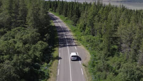 evergreen forest in iceland with white car driving on remote road, aerial