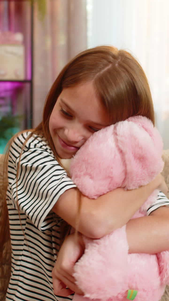 Bambina felice bambina che abbraccia il suo coniglietto preferito dolcemente con un sorriso mentre si siede sul comodo divano di casa