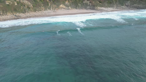 Aerial-drone-shot-approaching-a-group-of-surfers-enjoying-a-recreational-afternoon-riding-the-waves-at-Playa-de-Los-Locos-beach,-Suances,-Spain