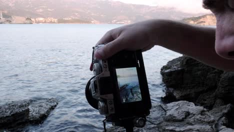 a man setting up his camera to photograph budva old town in montenegro with waves crashing in front of him during sunset