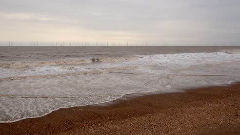 waves-rolling-onto-Ingoldmells,-Skegness-sandy-beach-and-wind-turbines-on-the-horizon