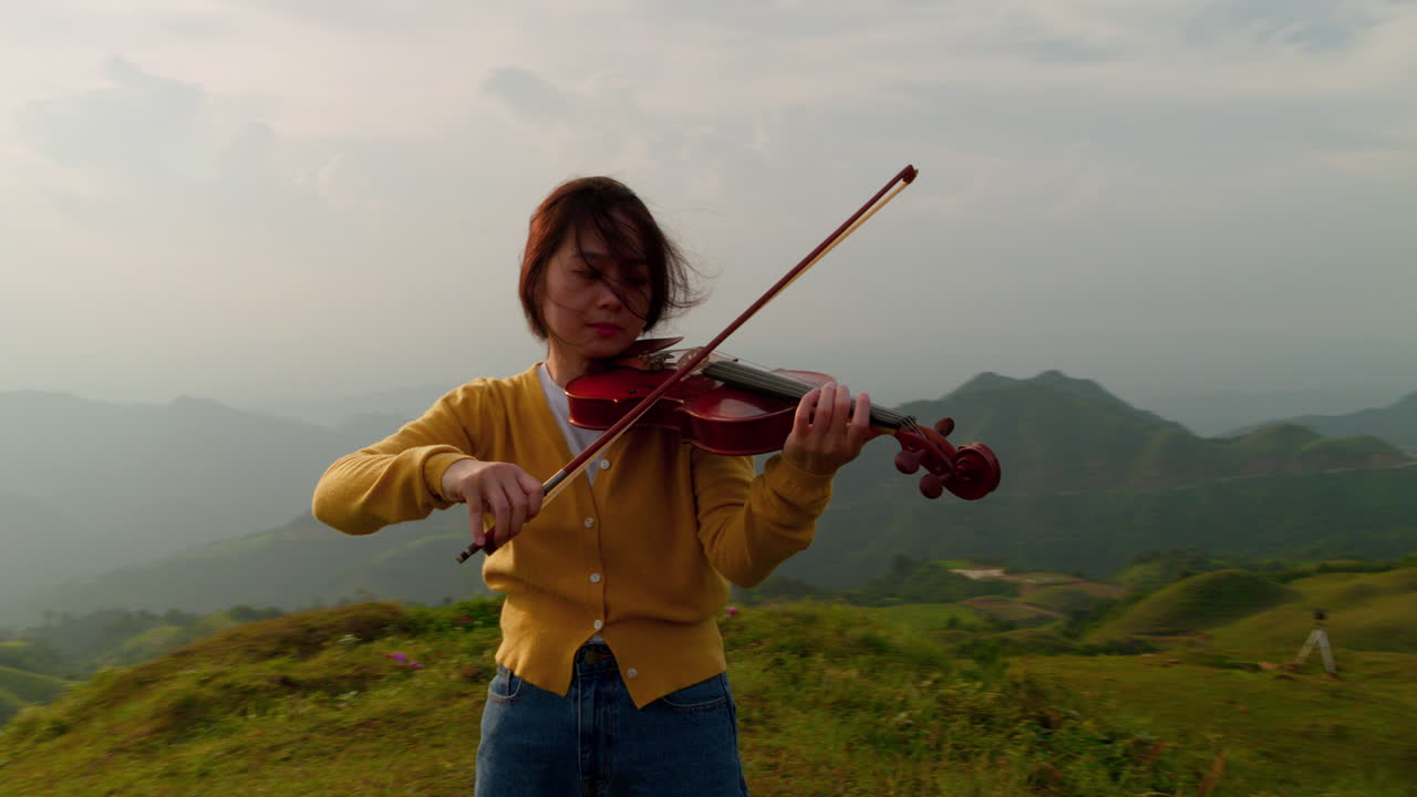 la cámara orbita a una mujer tocando el violín pacíficamente en una majestuosa ladera de una montaña en asia, un hermoso primer plano