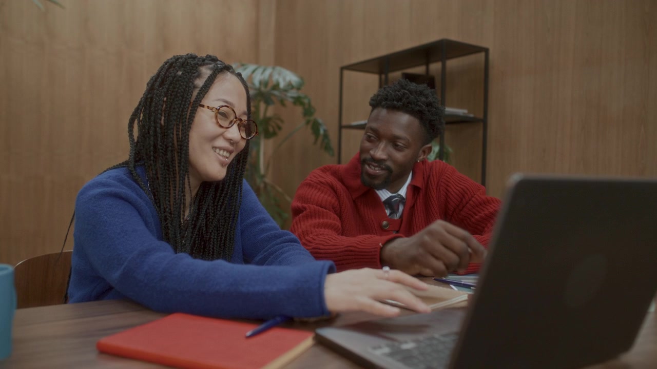 Asian Woman Using Laptop and Discussing Project with Black Coworker