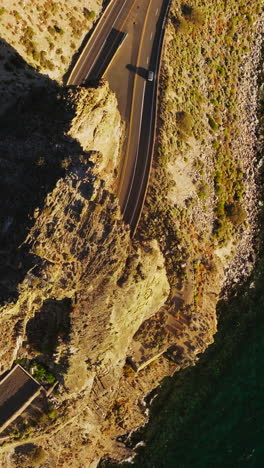 high rock with tunnels through it on the motorways. mountainous landscape of a lake shore on sunny day. top view. vertical video