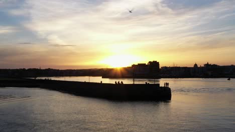 aerial view of the sea silhouettes of fishermen fishing along the docks of nimmo's pier are highlighted by the soft rays of sunrise in the background