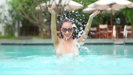 Primer-Plano-De-Una-Mujer-Joven-Juguetonamente-Salpicando-Agua-De-Piscina-En-El-Aire