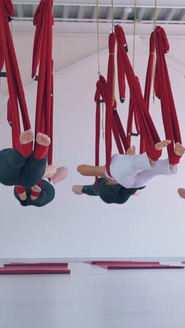 flexible women group relaxes after anti-gravity yoga workout and hangs in hammocks parallel to floor in stretching room