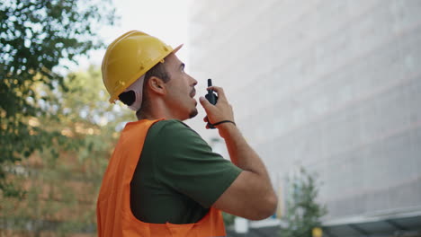 uniform engineer showing thumb talking walkie-talkie at urban district closeup