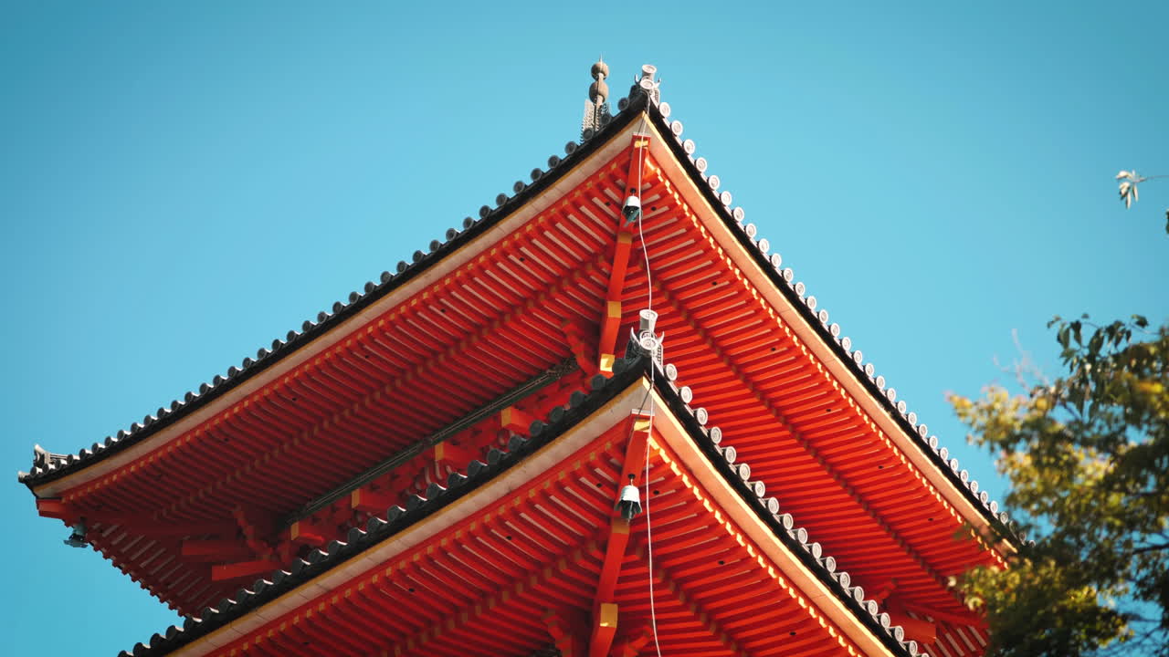 Traditional Japanese pagoda roof with intricate details at Kiyomizu-dera Temple, Kyoto with vibrant red color contrasts beautifully with the clear blue sky showcasing traditional Japanese architecture