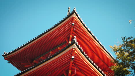 Traditional-Japanese-pagoda-roof-with-intricate-details-at-Kiyomizu-dera-Temple,-Kyoto-with-vibrant-red-color-contrasts-beautifully-with-the-clear-blue-sky-showcasing-traditional-Japanese-architecture