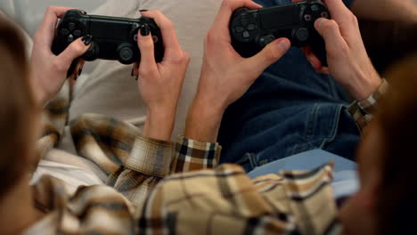 los jugadores con las manos sujetas a los gamepads descansan en casa de cerca. la pareja disfruta del videojuego.