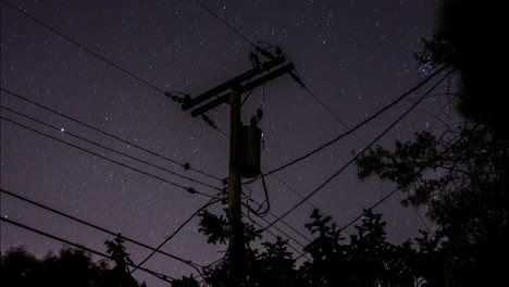 a time-lapse of the stars rotating in the sky behind a silhouetted suburban telephone pole and power lines and trees in the night sky
