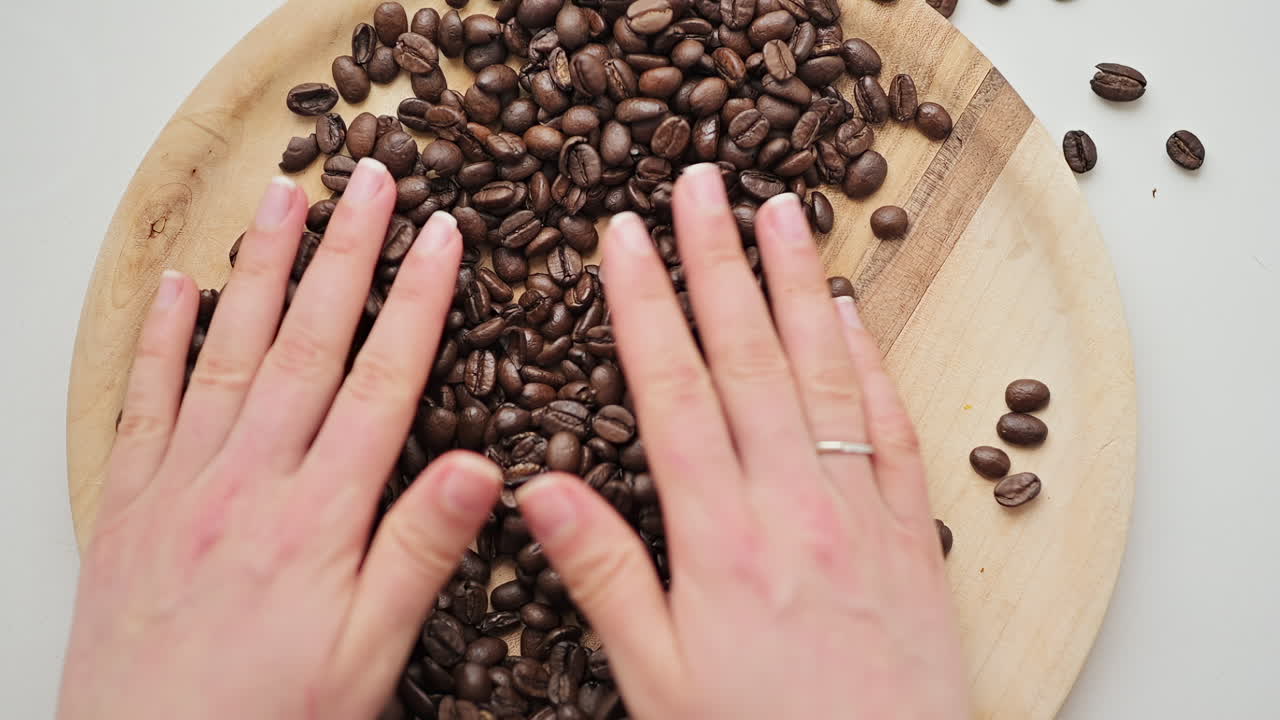 Hands touching and holding roasted coffee beans on a wooden tray