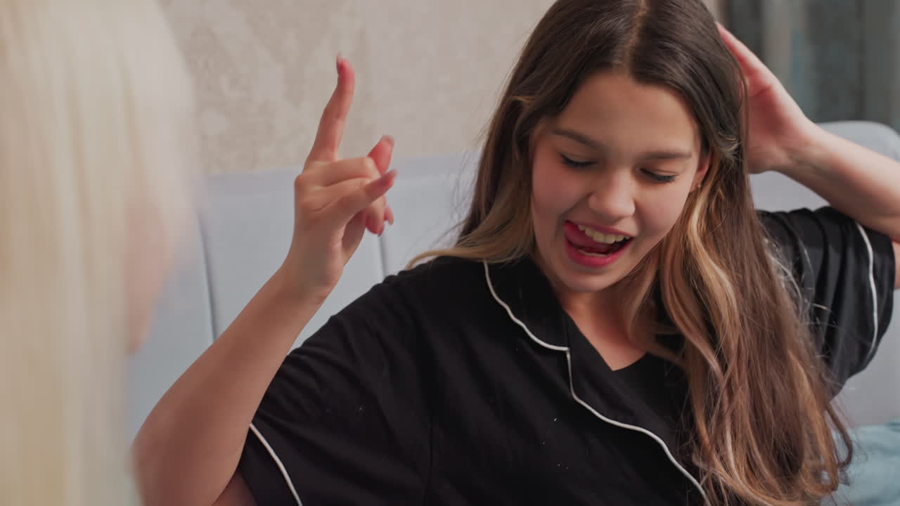 Smiling girl in black pajamas playfully throws popcorn at friend while sitting on bed, joyful moment captures candid interaction between friends in relaxed indoor setting