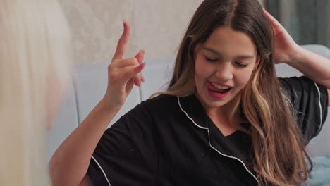 smiling girl in black pajamas playfully throws popcorn at friend while sitting on bed, joyful moment captures candid interaction between friends in relaxed indoor setting