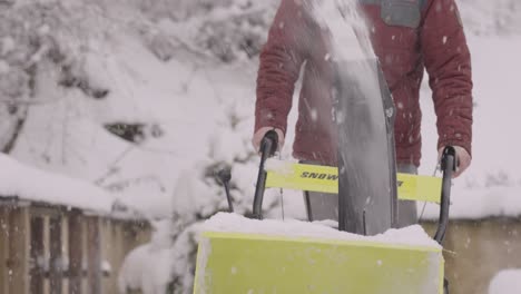 imágenes en cámara lenta de una persona empujando un soplador de nieve amarillo limpiando una entrada nevada