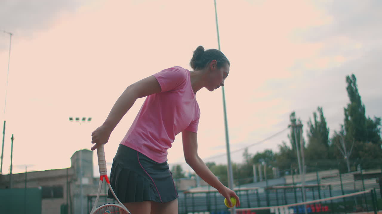 느린 움직임: 연습 중의 여성 스포츠 선수. 여자 운동 선수의 클로즈업이 테니스 공을 제공합니다. 젊은 여성은 일몰 때 테니스 라켓으로 공을 때리고 있습니다.