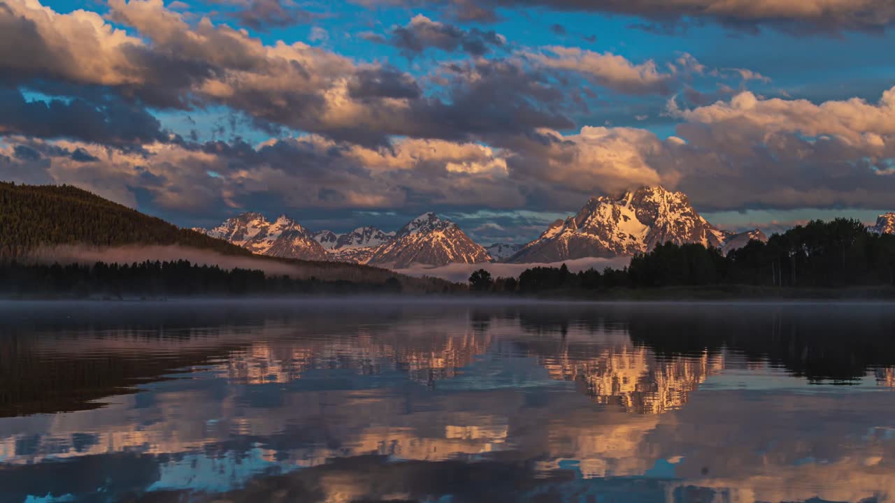 hermoso amanecer rosado y dorado en el lago espejo reflectante con montañas cubiertas de nieve y nubes gruesas que fluyen en el parque nacional grand teton, wyoming, estados unidos