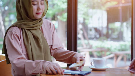 young beautiful asian muslim women enjoying a relaxing moment working and playing with mobile phone in the coffee shop on a bright sunny day