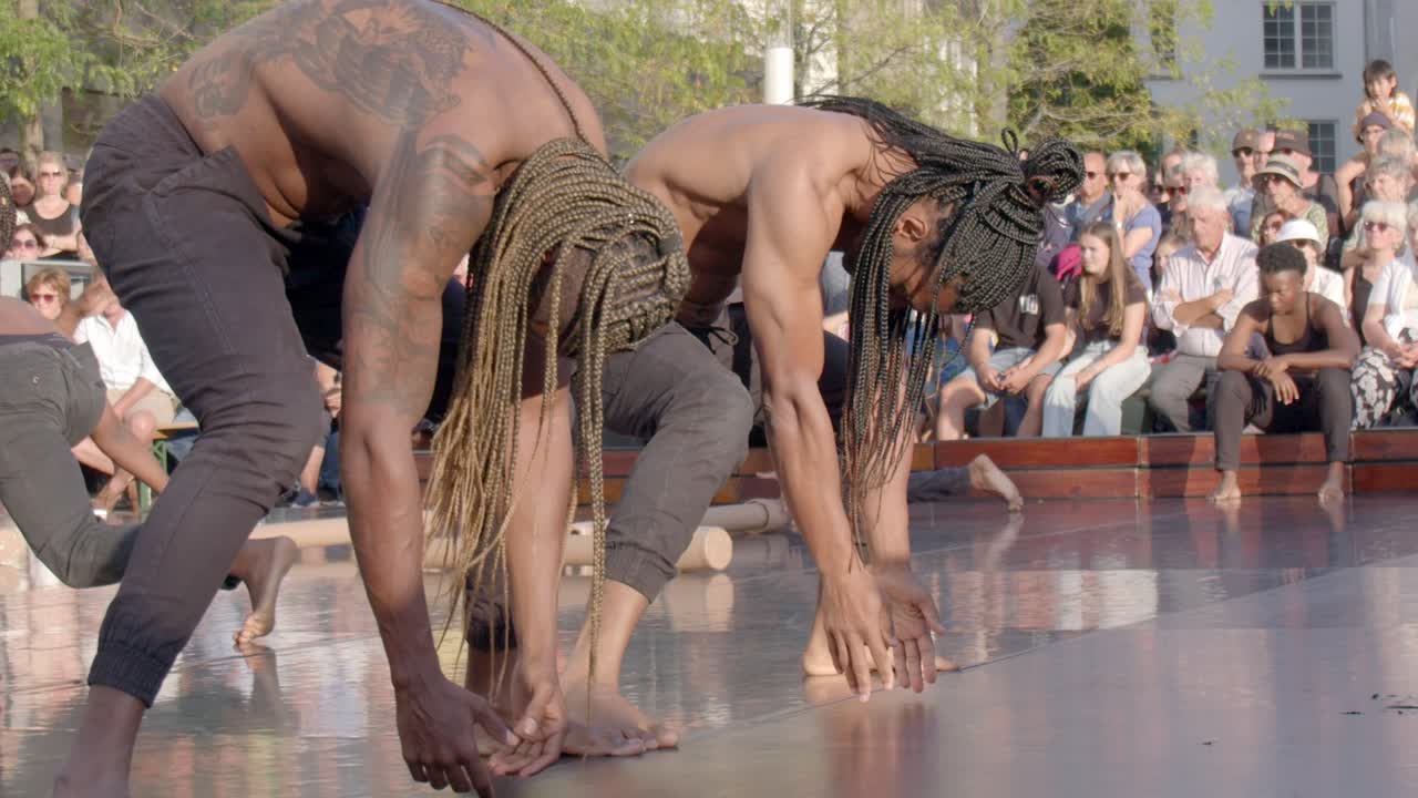 Young black African men with long braided hairstyle performing street dance during theatre festival, Handheld shot