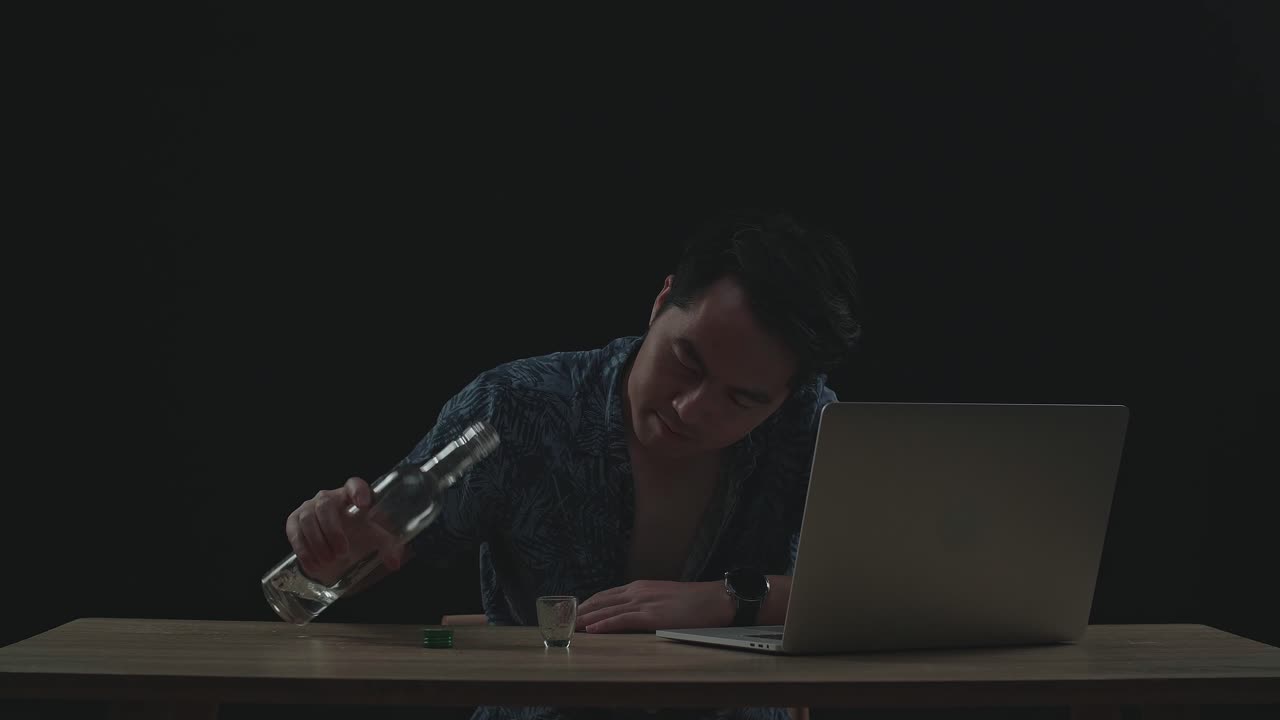 검은색 배경의 노트북에서 일하면서 보드카를 마시는 아시아인