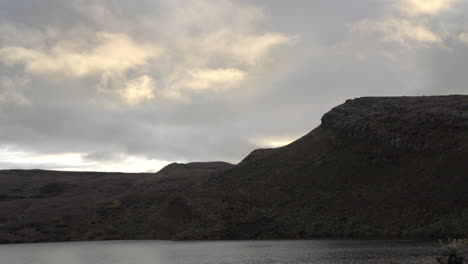 Wide shot of a calm mountain lake as clouds drift over a rocky ridge