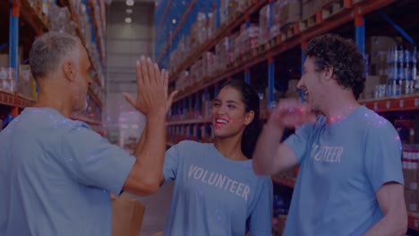 animation of glowing spots of light over diverse people high fiving volunteering in warehouse,