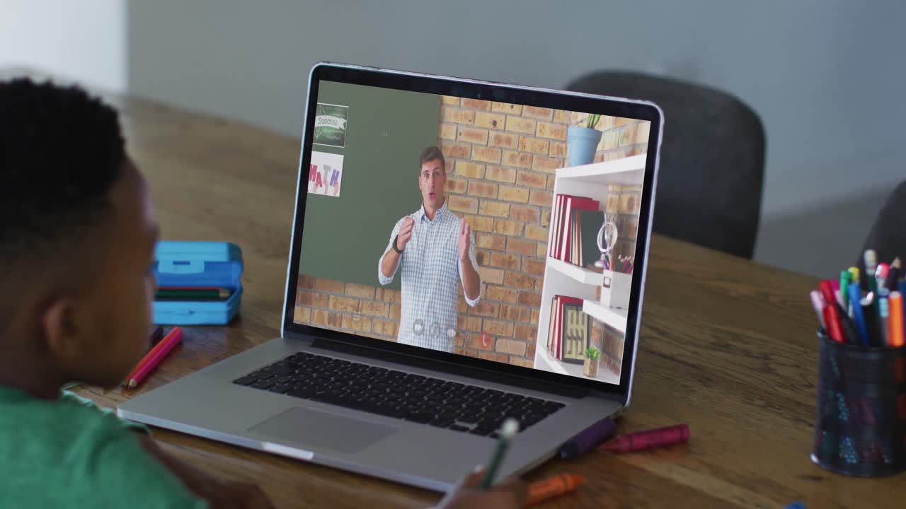 African american boy doing homework while having a video call with male teacher on laptop at home