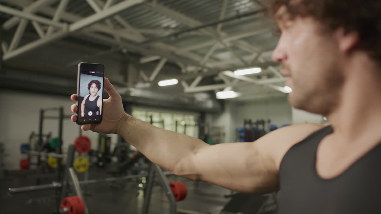 Muscular Man Filming Himself for Fitness Vlog with Phone in Gym