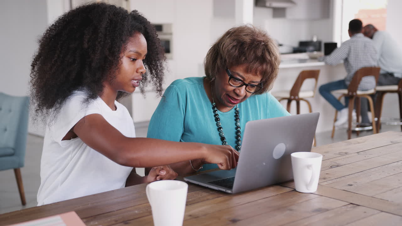 Teenage black girl helping her grandmother use a laptop computer at home, close up