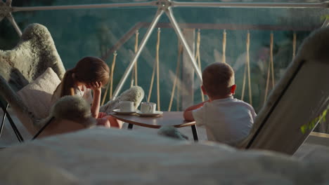 children look at landscape sitting at table. calm boy and girl enjoy silence of nature at dawn. little tourists relax in comfortable clear tent