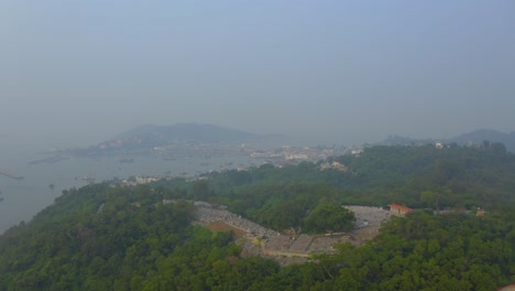 drone shot traveling forward above a forest on a hill toward a village on an island during a very polluted day.