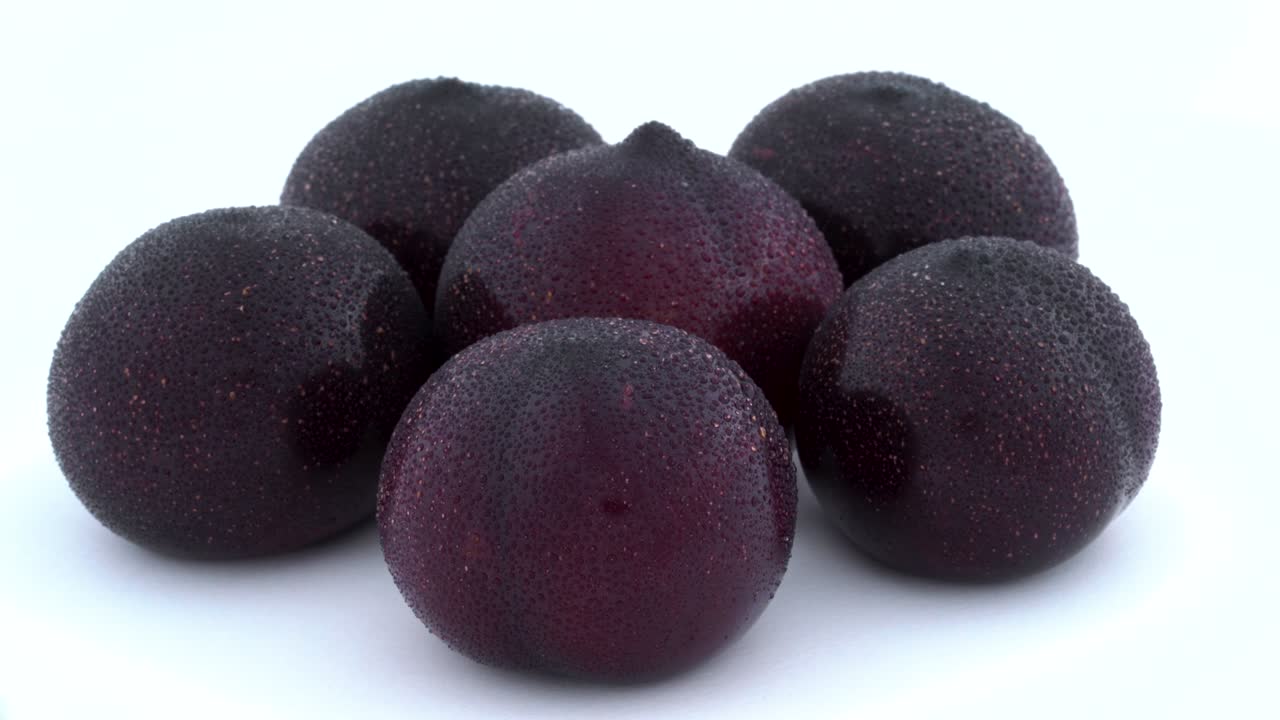 Few big purple plums rotating on the turntable. Water drops appears on the skin during rotation. Isolated on the white background. Close-up. Macro.