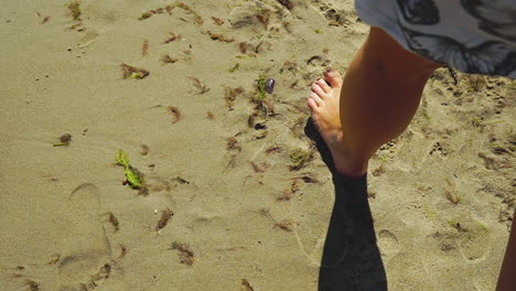 A-young-girl-goes-along-the-shore-of-the-beach,-you-can-only-see-a-piece-of-her-leg,-a-reflection-of-her-footprints-on-the-sand