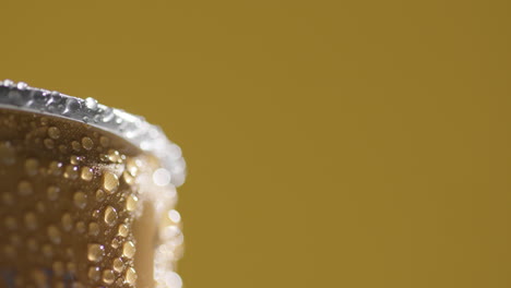 close up of condensation droplets on revolving takeaway can of cold beer or soft drink against yellow background with copy space