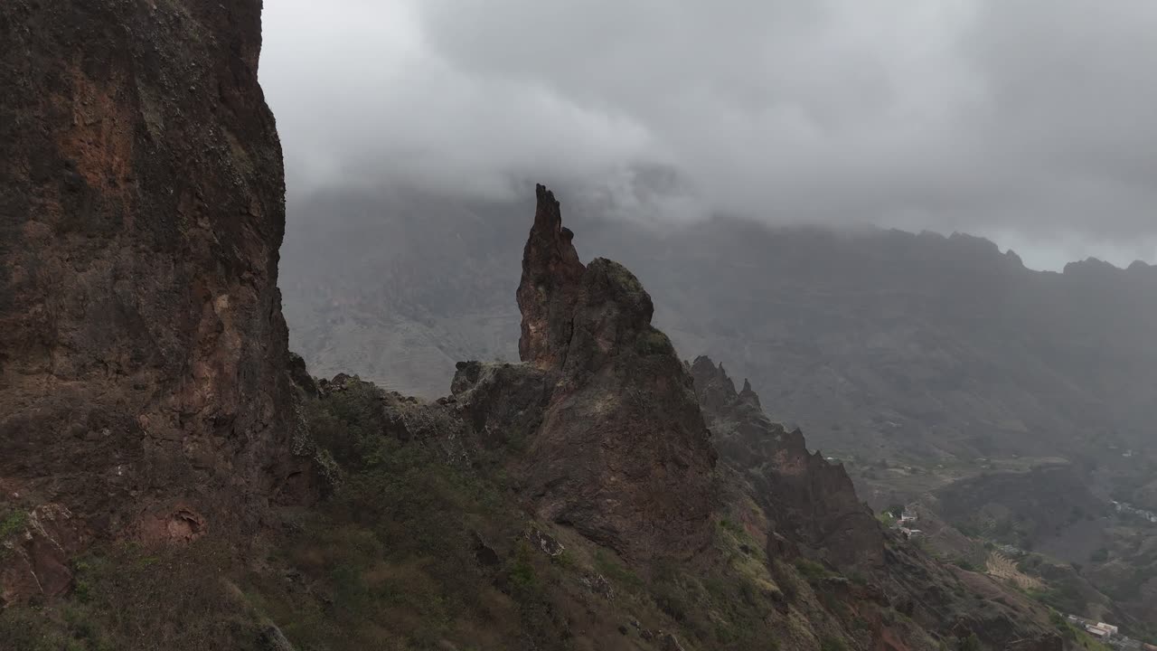 Espectacular toma aérea de un afilado pináculo de roca basáltica emergiendo de las montañas brumosas de Santo Antão, Cabo Verde. Formación geológica única en un entorno de tierras altas volcánicas escarpadas