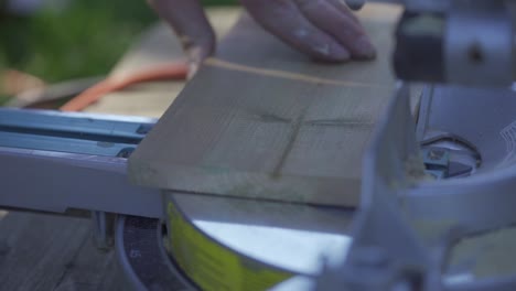 man's hands placing and cutting wooden plank on mitre saw, close up slow motion