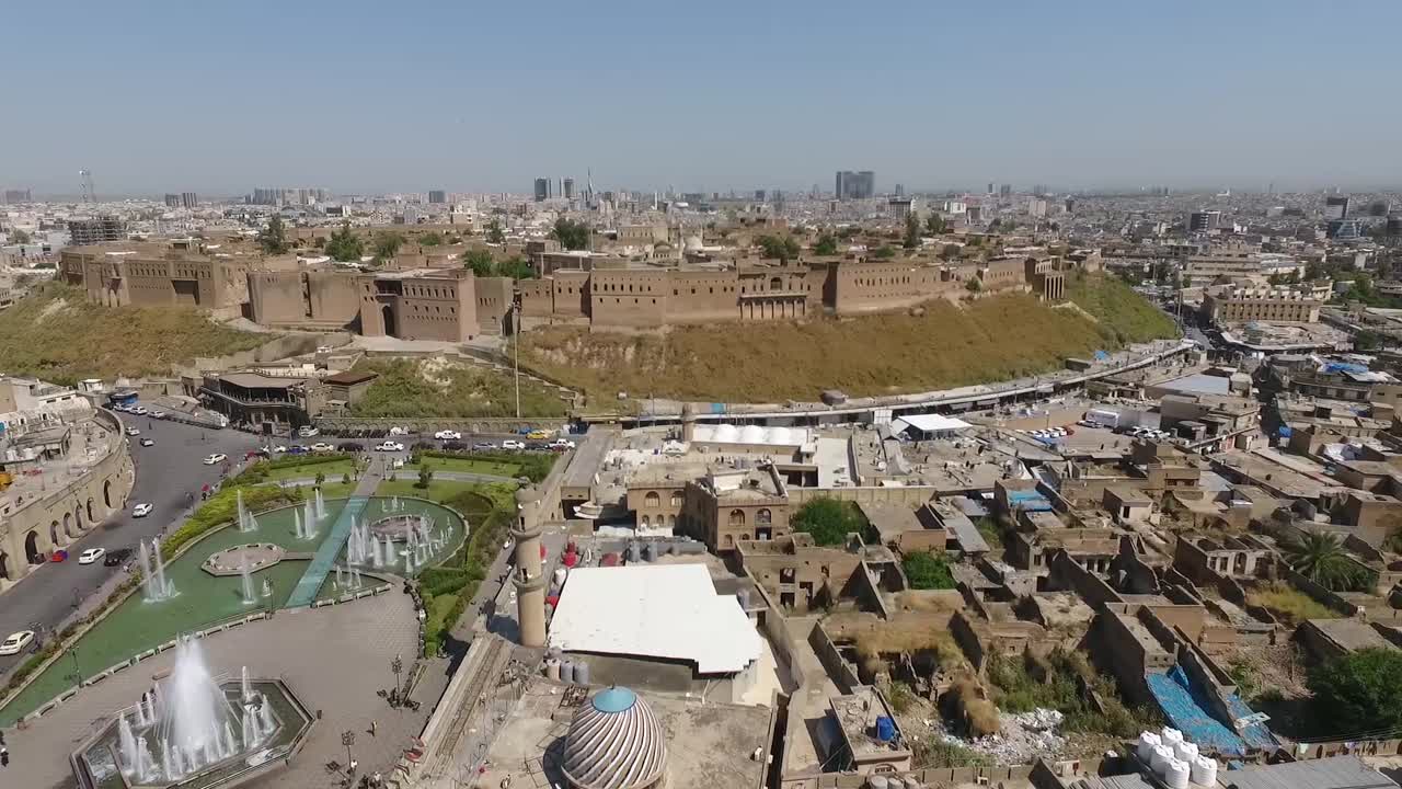 una toma aérea de la ciudad de erbil que muestra la antigua ciudadela de erbil y el jardín frente al castillo con fuentes de agua y el mercado popular