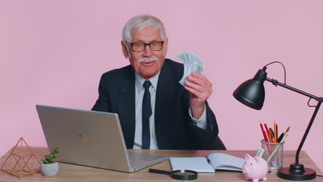 Senior-business-office-man-analyzes-financial-charts-celebrate-success-win-at-home-workplace-desk