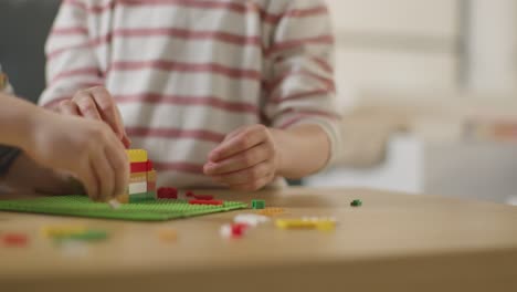 Close-Up-Of-Two-Children-Playing-With-Plastic-Construction-Bricks-On-Table-At-Home-4