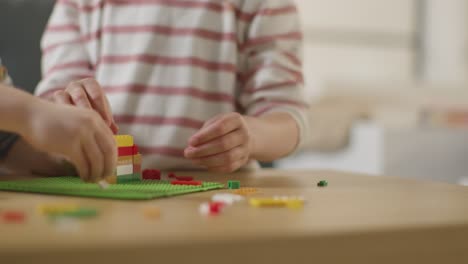 cerca de dos niños jugando con ladrillos de construcción de plástico en la mesa en casa 4