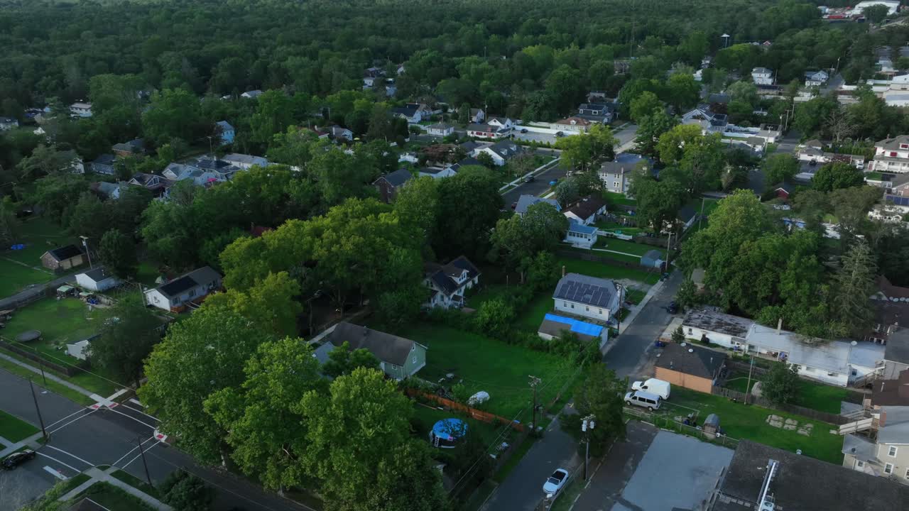 American neighborhood with single family houses and green garden. Aerial backwards shot. Main Street with traffic. Dusk scene in summer. Wide shot. Buildings and homes in small quiet town