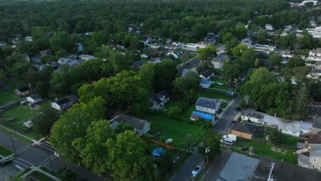 american neighborhood with single family houses and green garden. aerial backwards shot. main street with traffic. dusk scene in summer. wide shot. buildings and homes in small quiet town