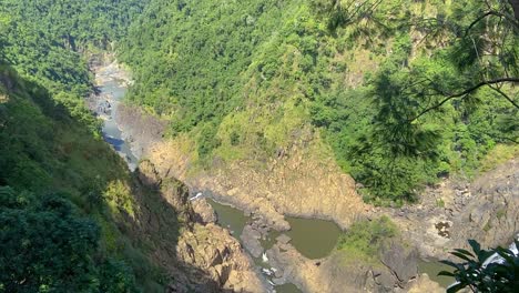 Smooth-slow-panning-shot-along-the-rocky-pools-of-the-Barron-river,-following-the-deep-valley-to-reveal-the-stunning-vista-of-the-dense-tropical-rain-forest-shrouded-mountains-of-North-Queensland