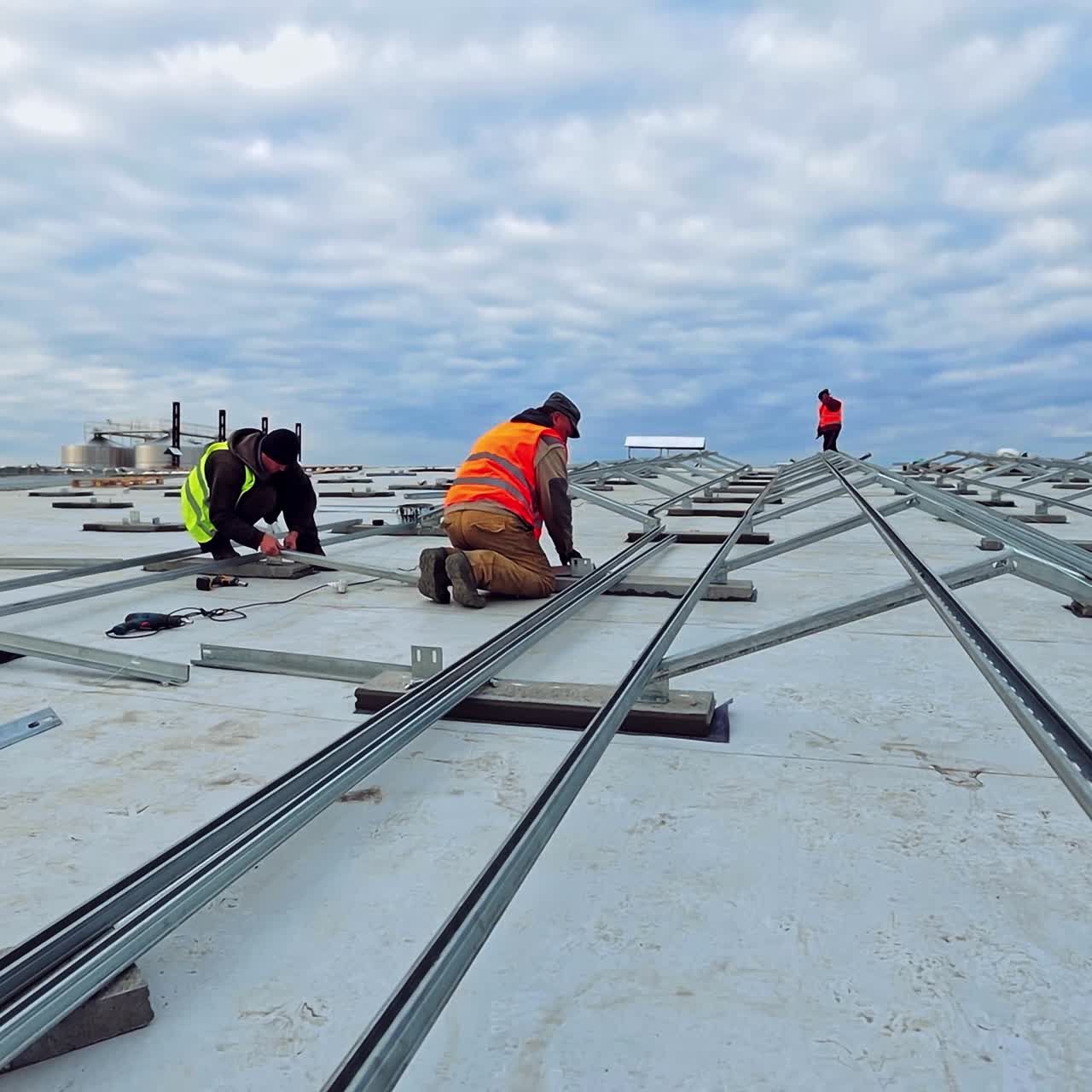 Installation of innovative solar farm under the blue sky. Metal basis for solar panels on roof. Workers in uniform construct base for photovoltaic cells.