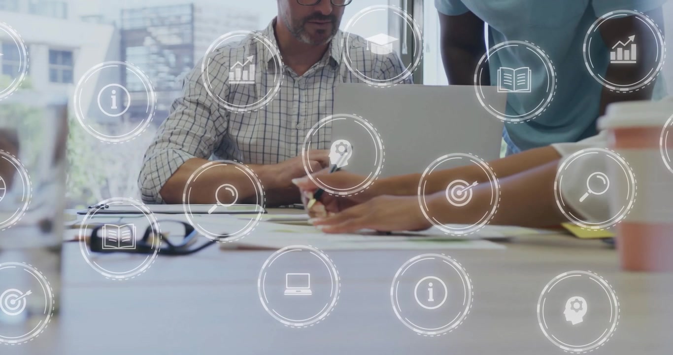 Senior man tapping laptop and showing floating business icons while colleagues reviewing documents