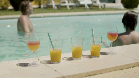 cerca de jugos de naranja y cócteles junto a la piscina mientras que en el fondo una familia feliz jugando con la pelota en la piscina