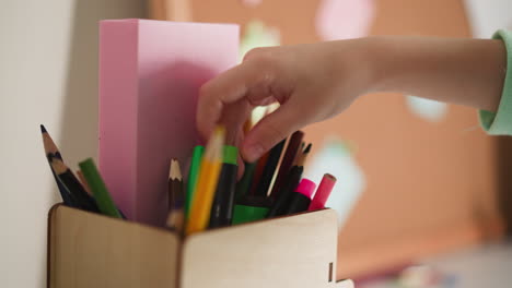 girl chooses pencil for drawing in wooden holder on table