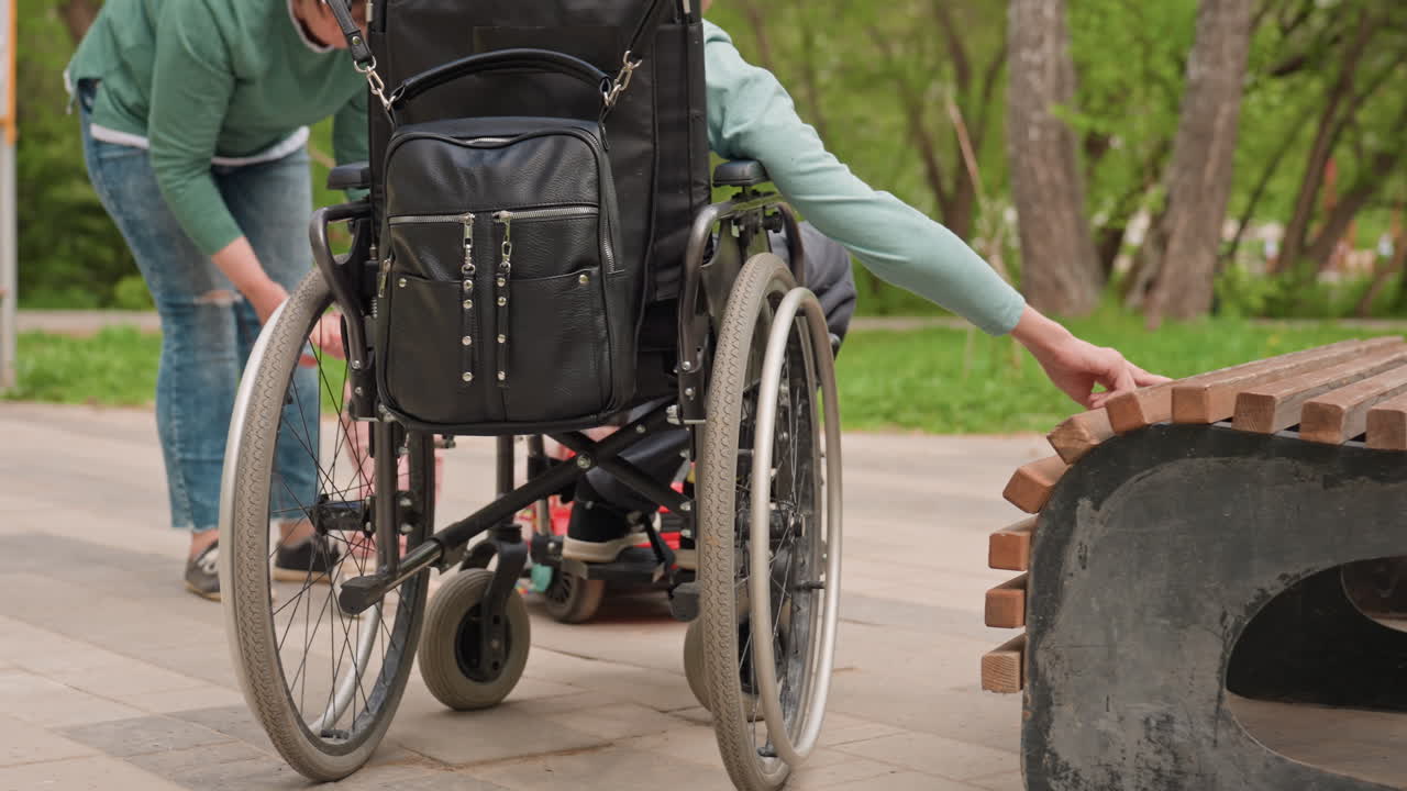 Caucasian Mother Guides Toddler Near Park Bench, Family Inclusion As Mother Assists Young Child With Support, Gentle Guidance From Mother Helps Toddler Take First Steps By Park Walkway