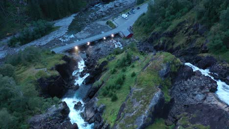 Spitze-Des-Latefoss-Wasserfalls-Mit-Blick-Auf-Straße-Und-Brücke-Mit-Lichtern-In-Der-Abenddämmerung---Nach-Unten-Bewegte-Antenne-In-Der-Mitte-Des-Wasserfalls